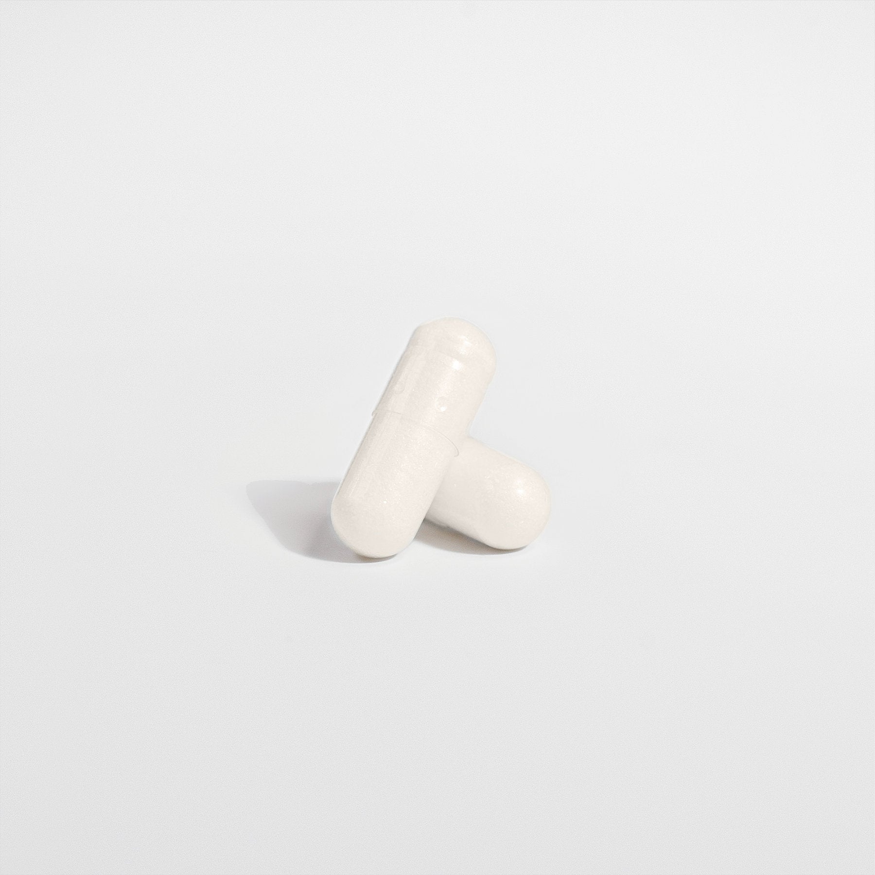 Two white Healthy8Always 5-HTP capsules stand upright on a white background, casting a soft shadow. These supplements may support serotonin levels and enhance emotional well-being.