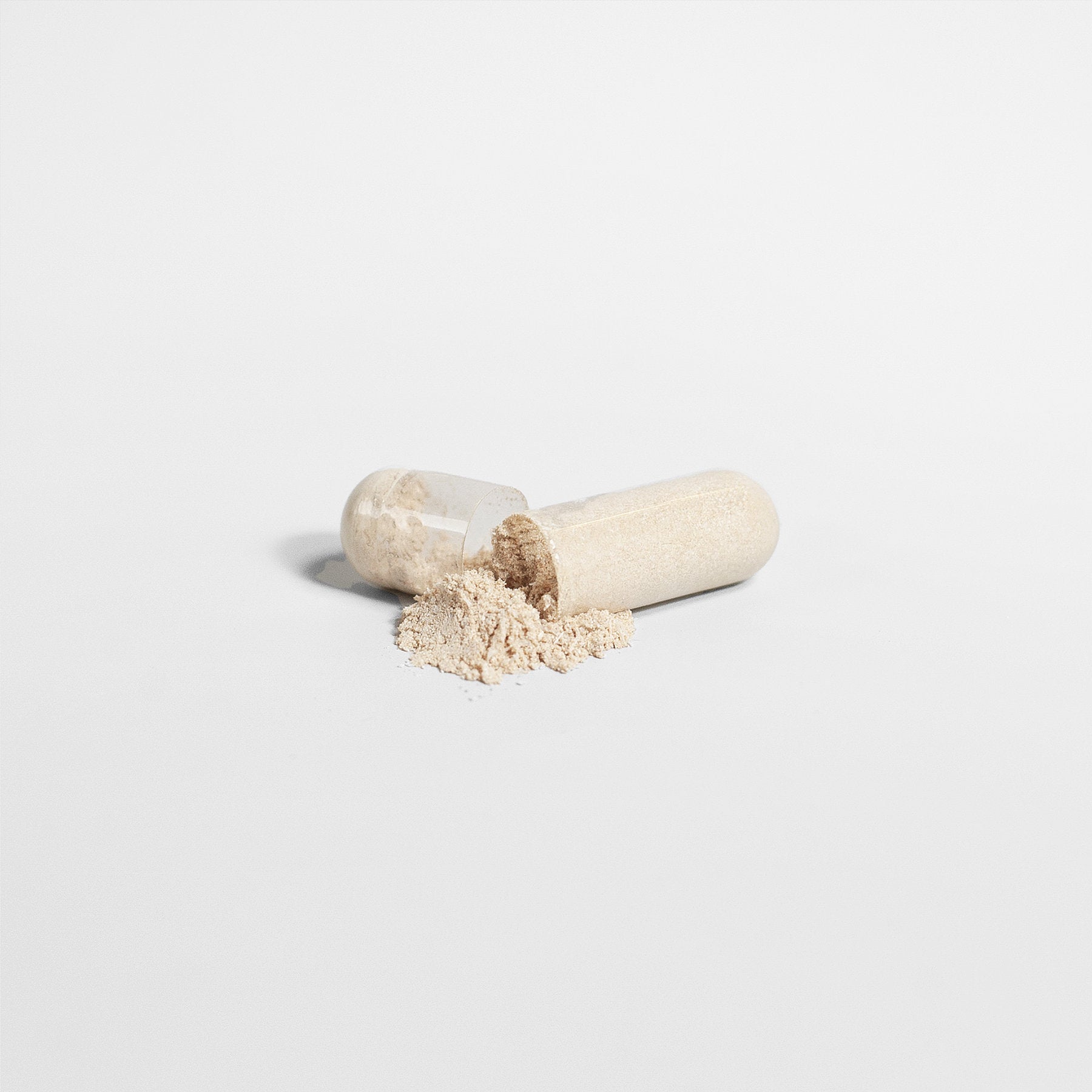 A Sea Moss capsule from Healthy8Always split open, revealing beige powder spilling out against a plain white background.